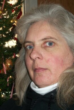 A woman posing indoors near a decorated Christmas tree.