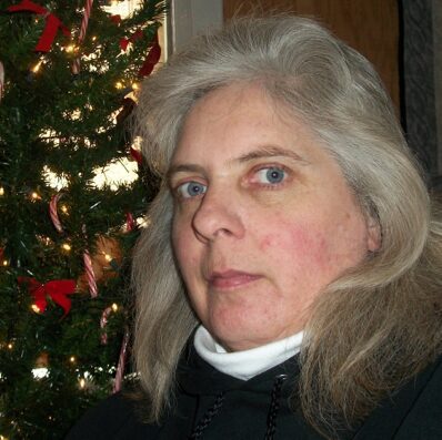 A woman posing indoors near a decorated Christmas tree.