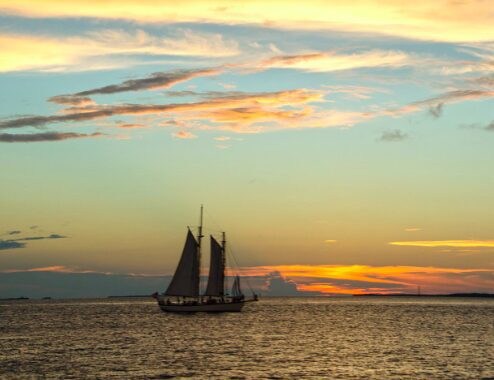 Sailboat glides on calm ocean at sunset with vibrant sky.