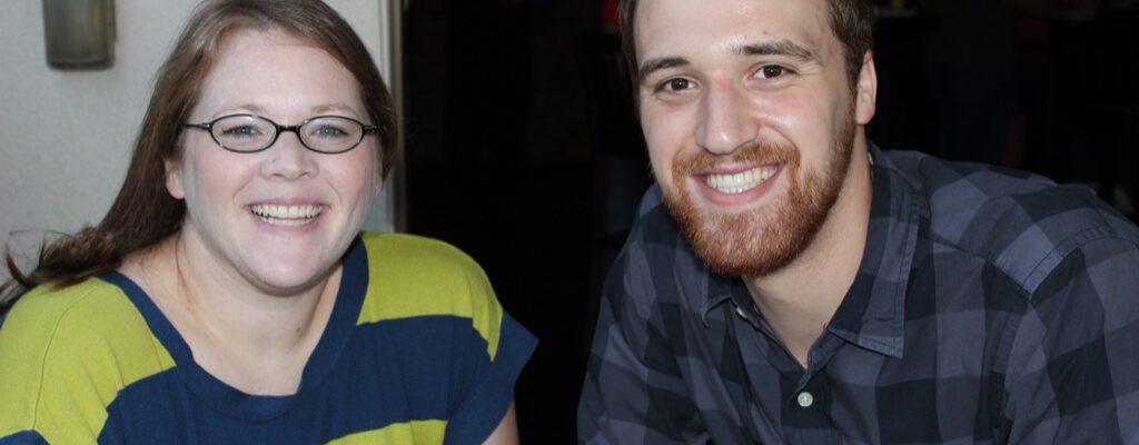 Two smiling people sitting together indoors, enjoying the moment.