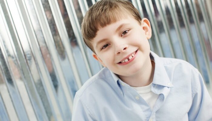 Smiling young boy with braces wearing a light blue shirt.