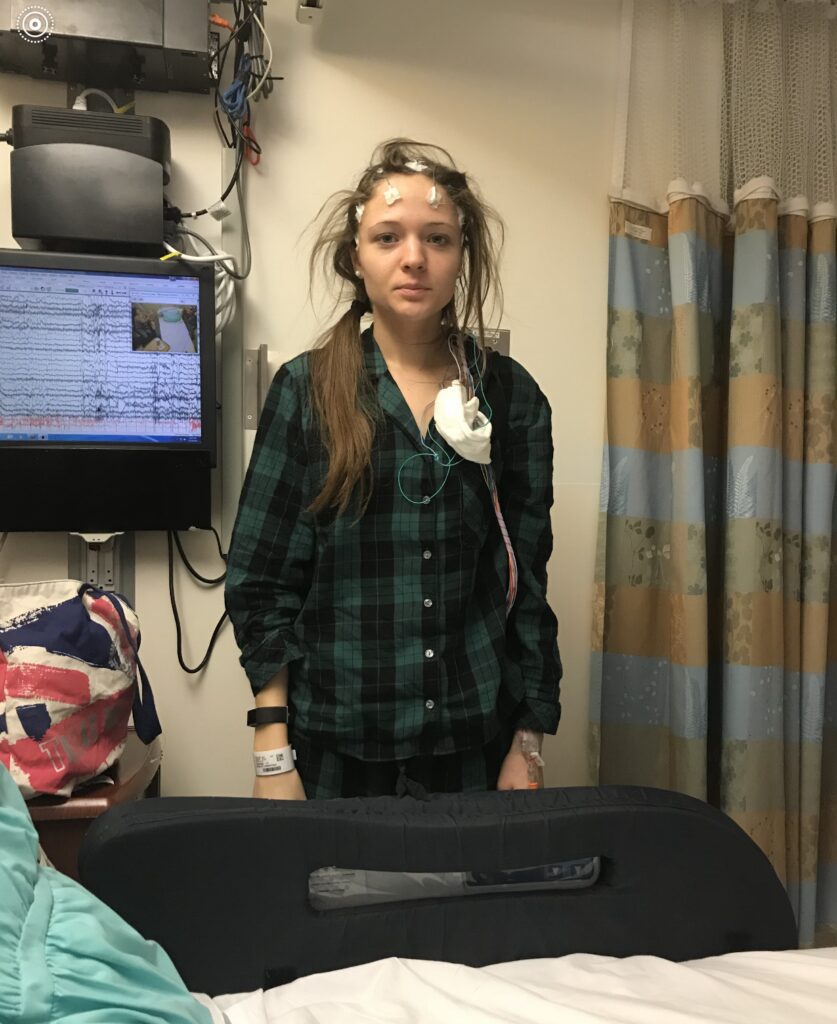 Young woman in a hospital room wearing an plaid shirt and medical monitoring equipment.