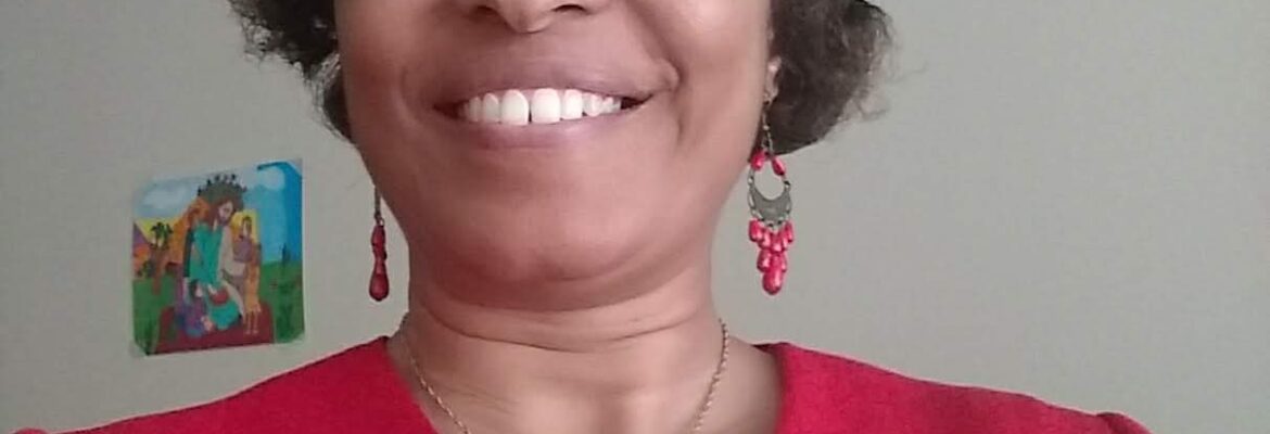 Smiling woman wearing glasses and a red top with a cross necklace.