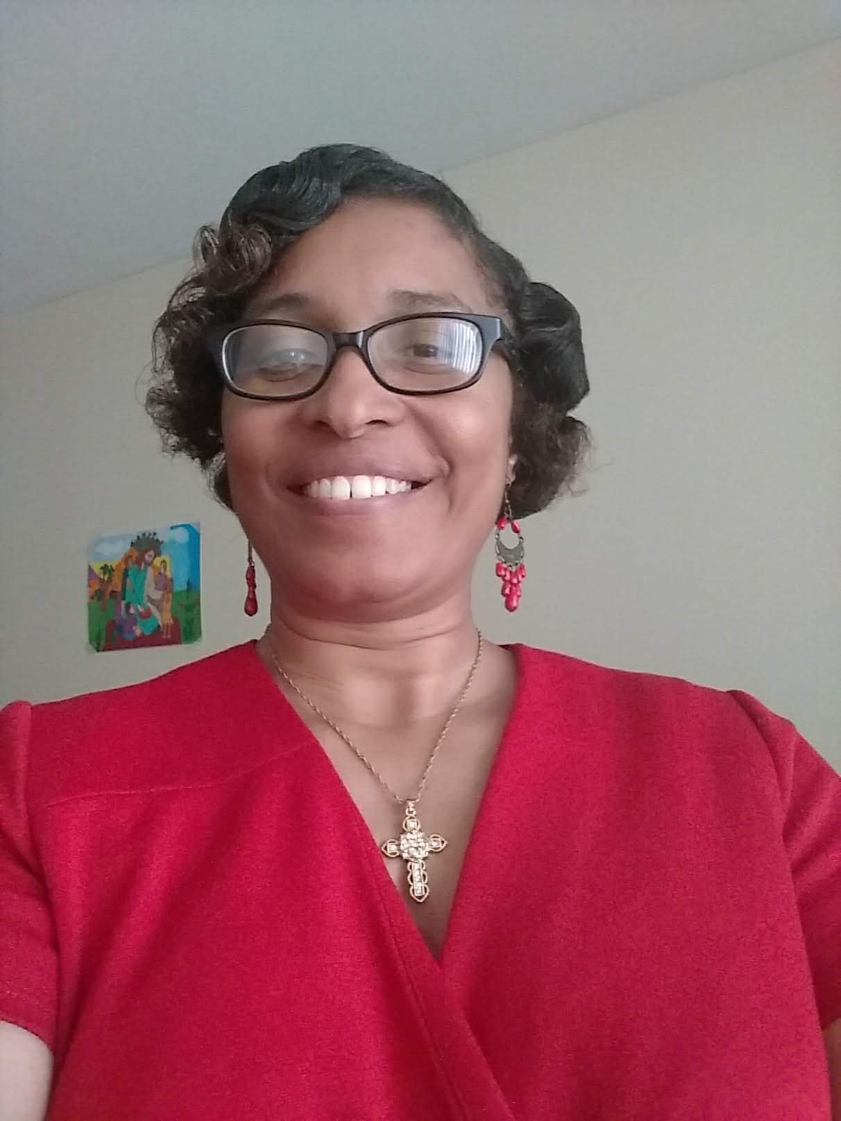 Smiling woman wearing glasses and a red top with a cross necklace.