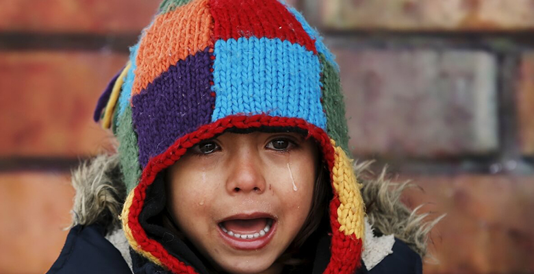 A child wearing a colorful knit hat with a distressed expression.