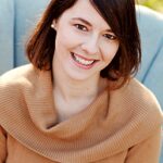 Smiling woman with short brown hair and a cozy tan sweater.