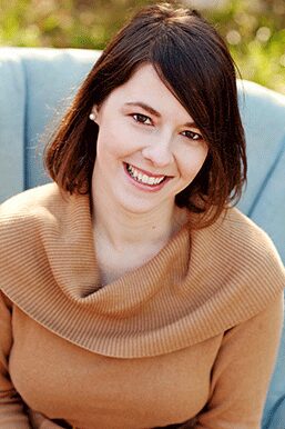 Smiling woman with short brown hair and a cozy tan sweater.