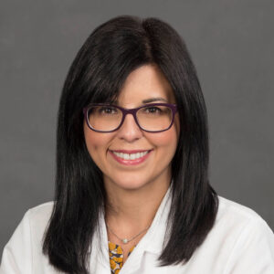 Professional woman in white coat with glasses smiling.