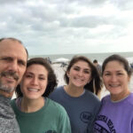 Family smiling on a cloudy beach day.