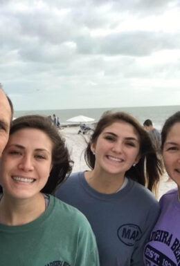 Family smiling on a cloudy beach day.