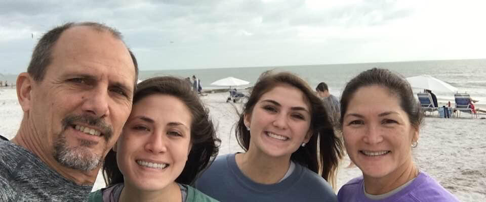 Family smiling on a cloudy beach day.