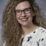 Smiling woman with curly hair and glasses.