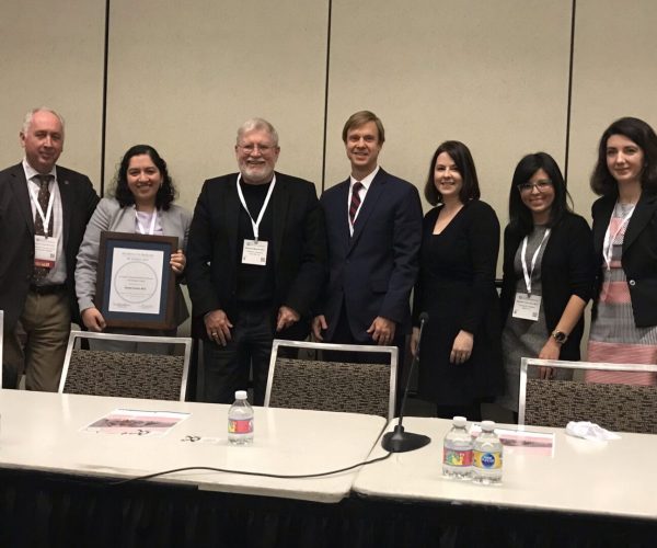 Group of six professionals posing at a conference panel table.