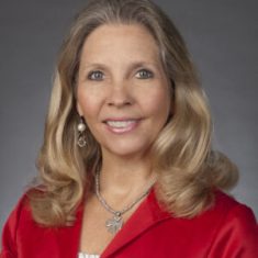 Smiling woman with blonde hair in a red top against a gray background.