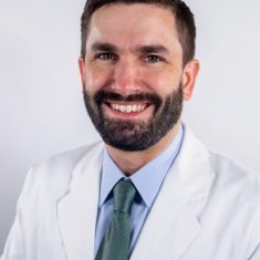 Smiling man in a white medical coat.