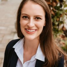 A smiling woman with long brown hair wearing a black blazer and white shirt.