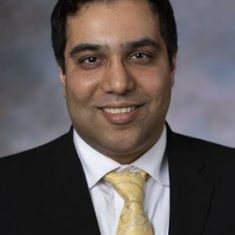 Professional headshot of a man wearing a suit and yellow tie.