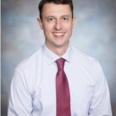 Professional man in white shirt and red tie smiling at the camera.