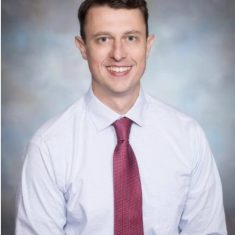 Professional man in white shirt and red tie smiling at the camera.